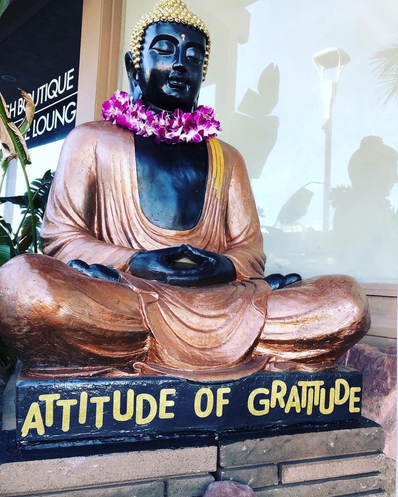Buddha statue with orchid lei and Attitude of Gratitude sign at Bikram Yoga El Paseo hot yoga studio.